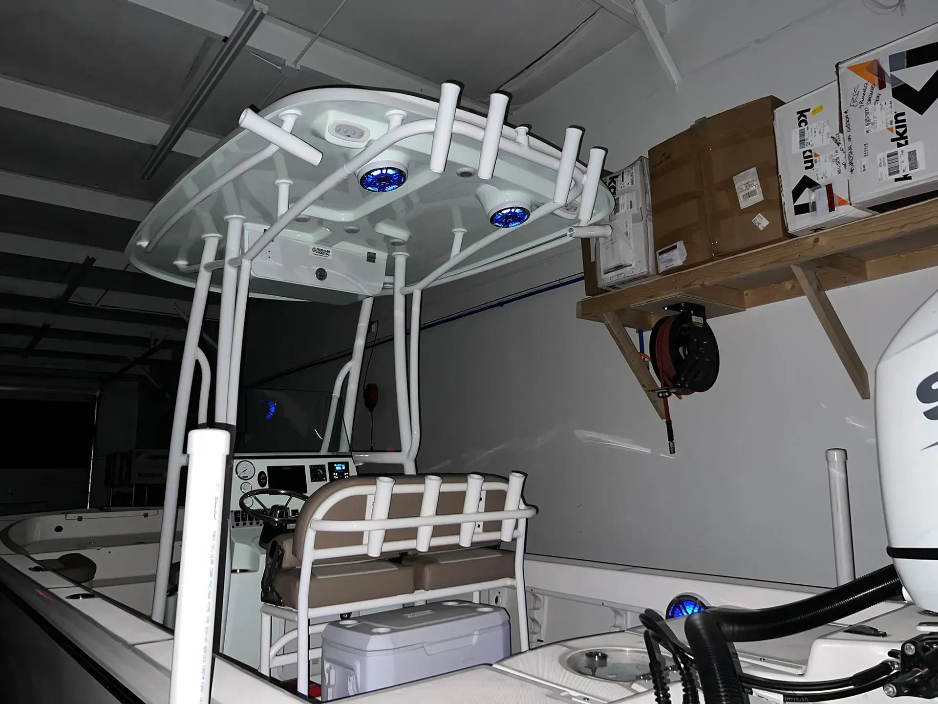 White fishing boat with a T-top in a workshop setting, boxes on a shelf.