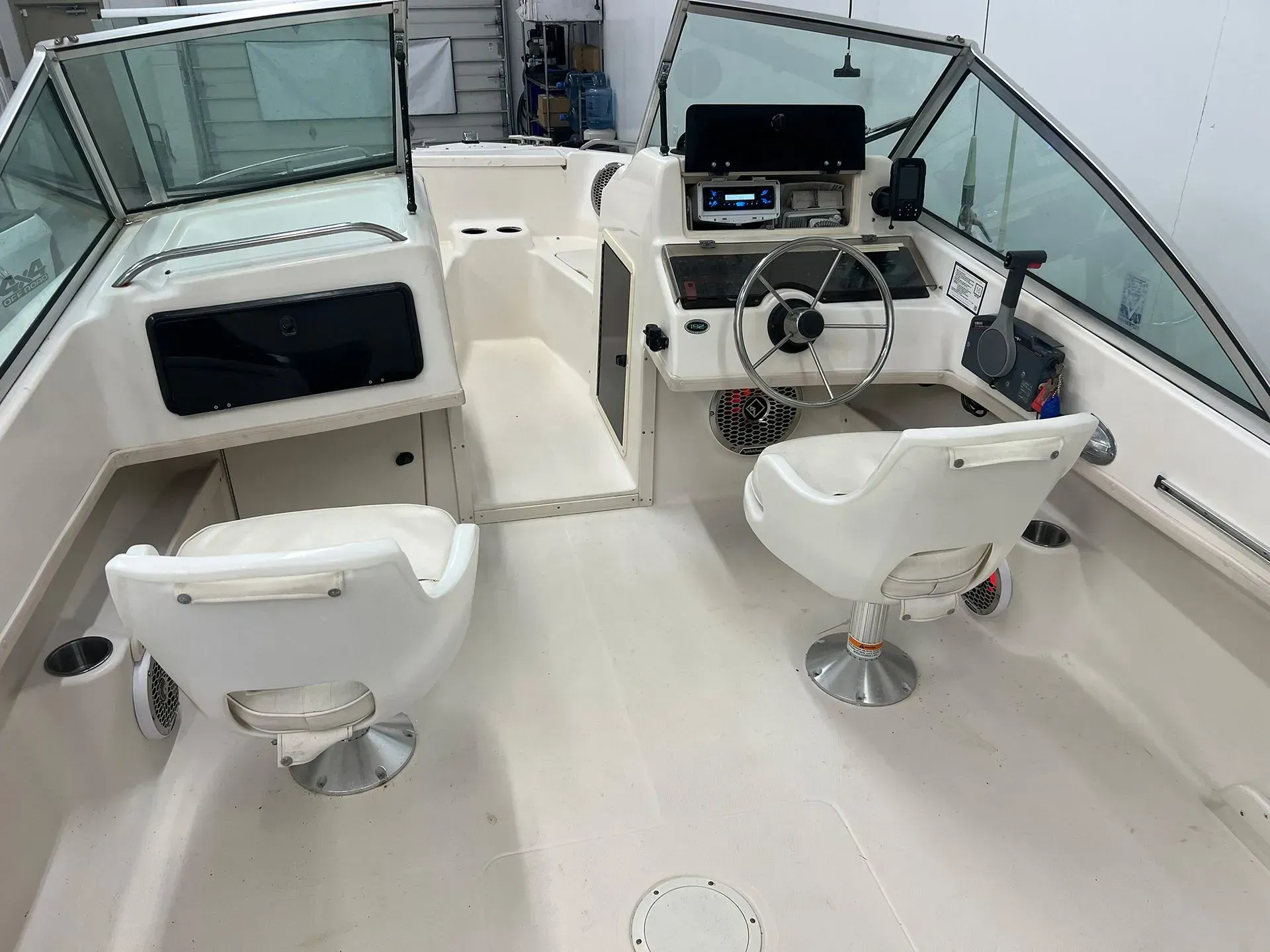 Interior of a boat with two white captain's chairs, a steering wheel, and navigation instruments.