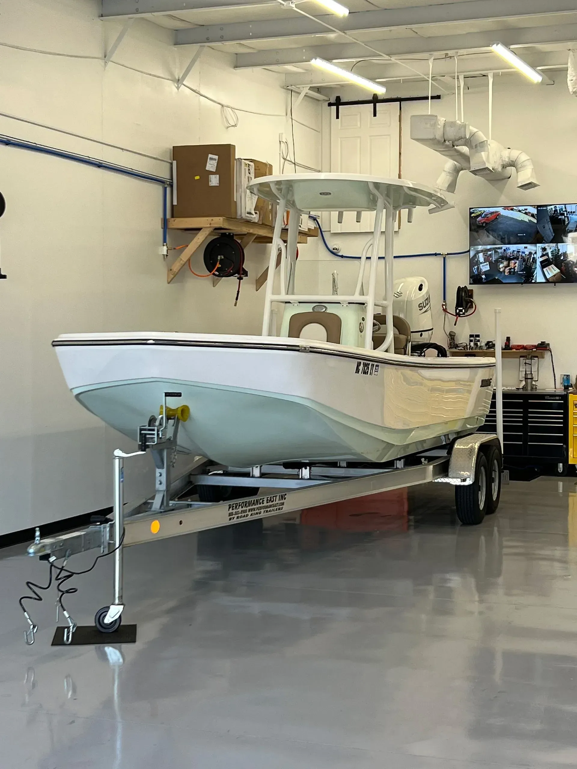 Boat on a trailer inside a workshop, white hull, blue trim, and a white tower.