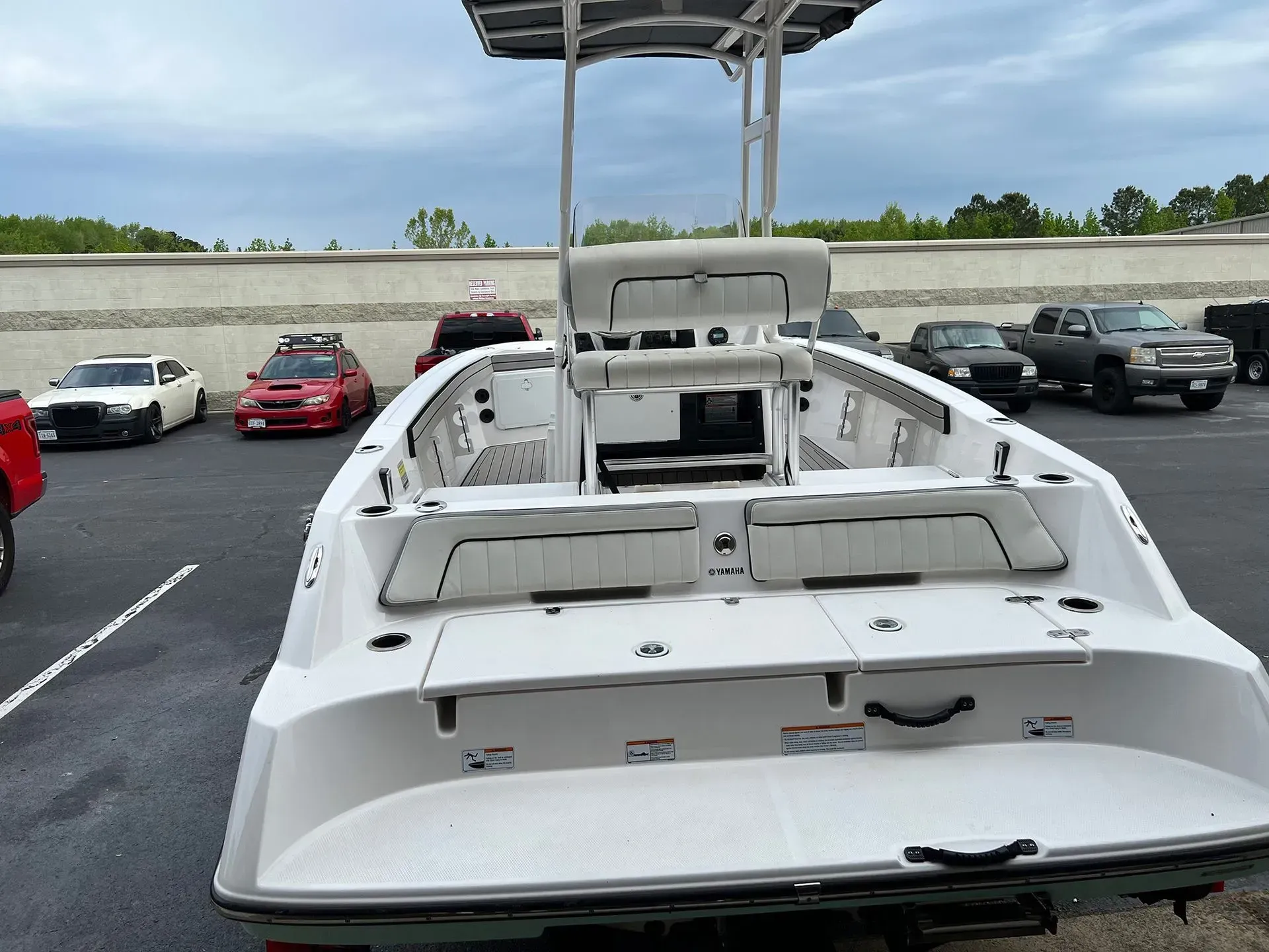 White motorboat in a parking lot, with a canopy. Cars are parked in the background, under a cloudy sky.