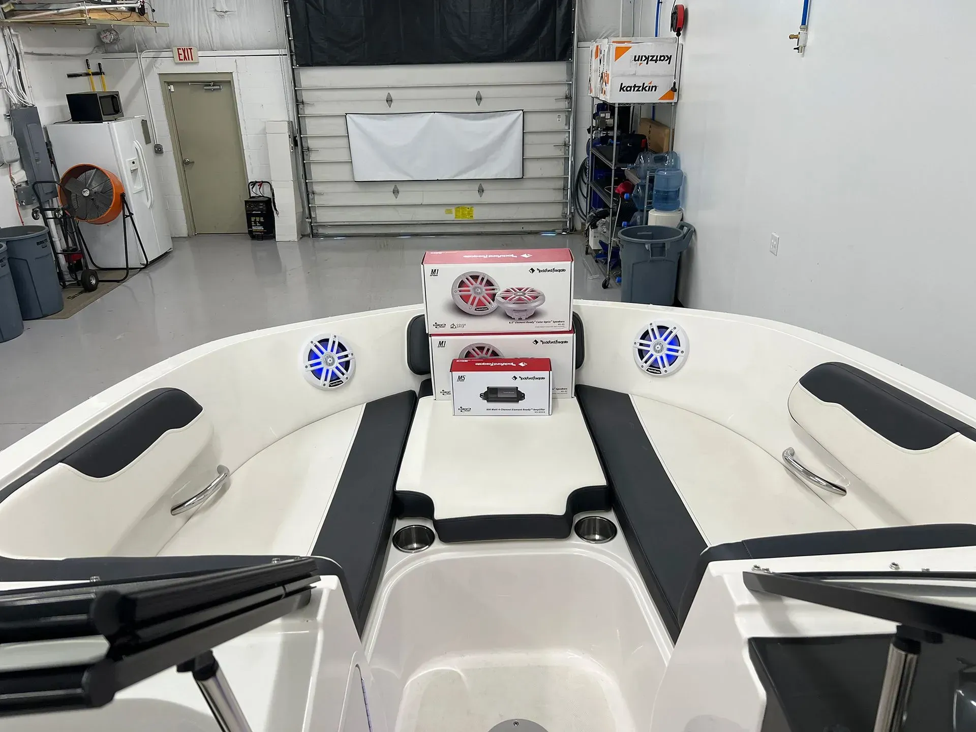 Boat interior with stereo components on a white and black surface. Speakers are visible. Workshop background.