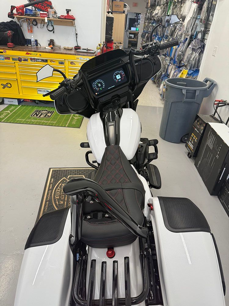 White and black custom motorcycle in a garage, features digital display, carbon fiber accents, and blacked-out components.