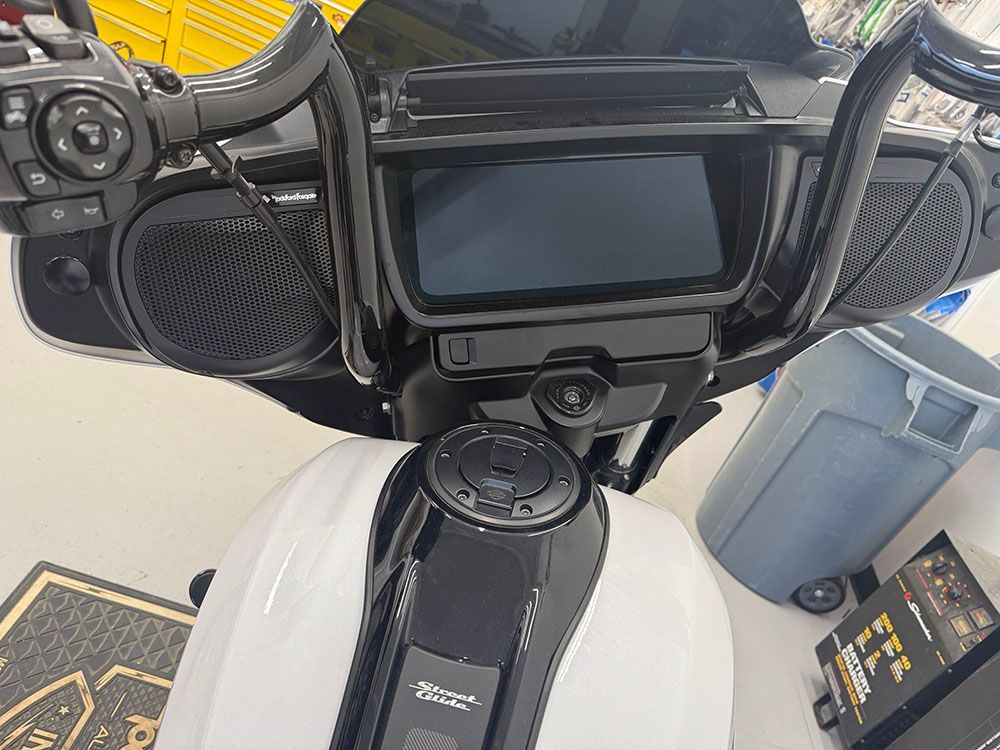 Black motorcycle handlebars, screen, speakers, and white gas tank.