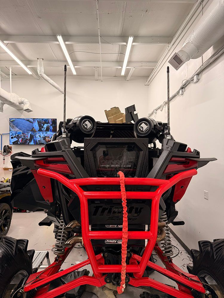 Red and black ATV with a roll cage, lights, and two antennas indoors.