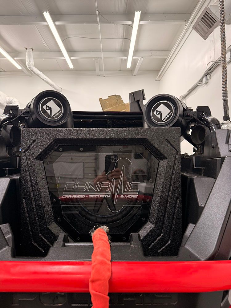 Close-up of black and red off-road vehicle with roll cage. Two speakers with logos face the viewer.