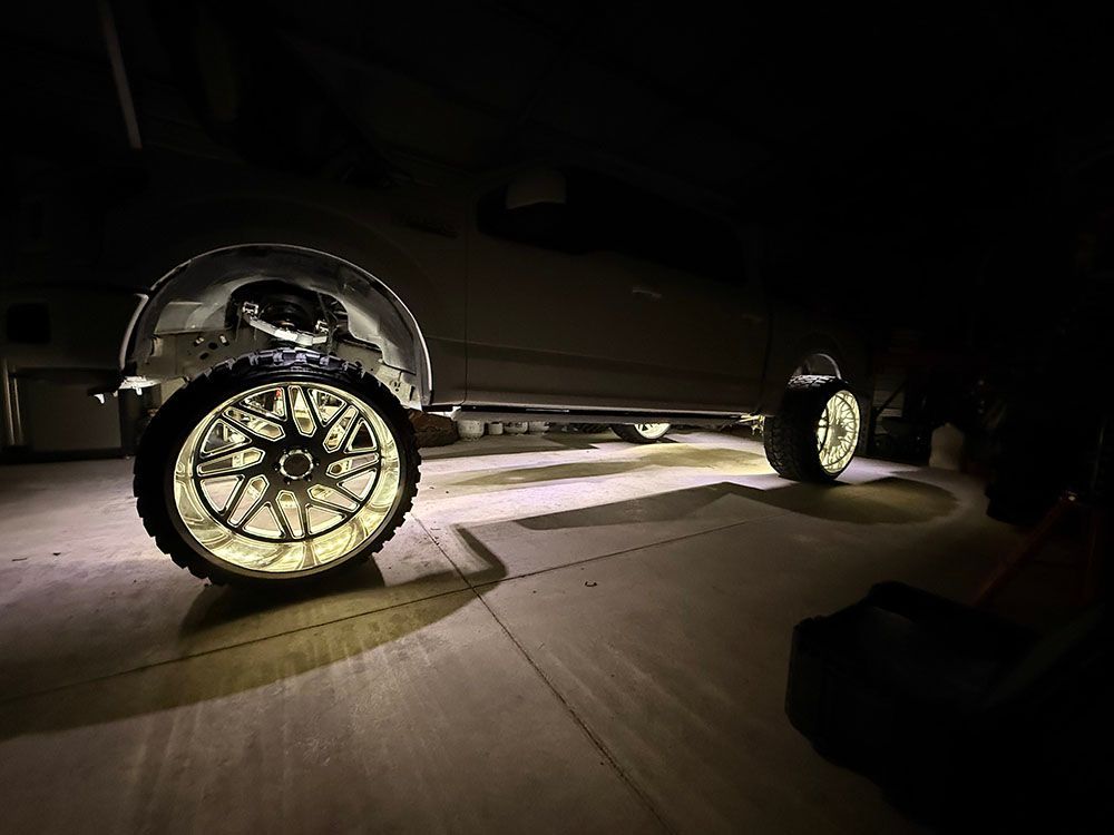 Truck with underglow and illuminated chrome wheels in a garage.