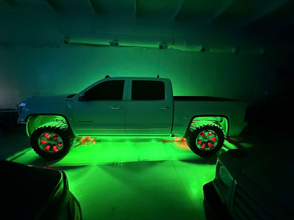 White pickup truck with green underglow and red wheel lights in a dark space.
