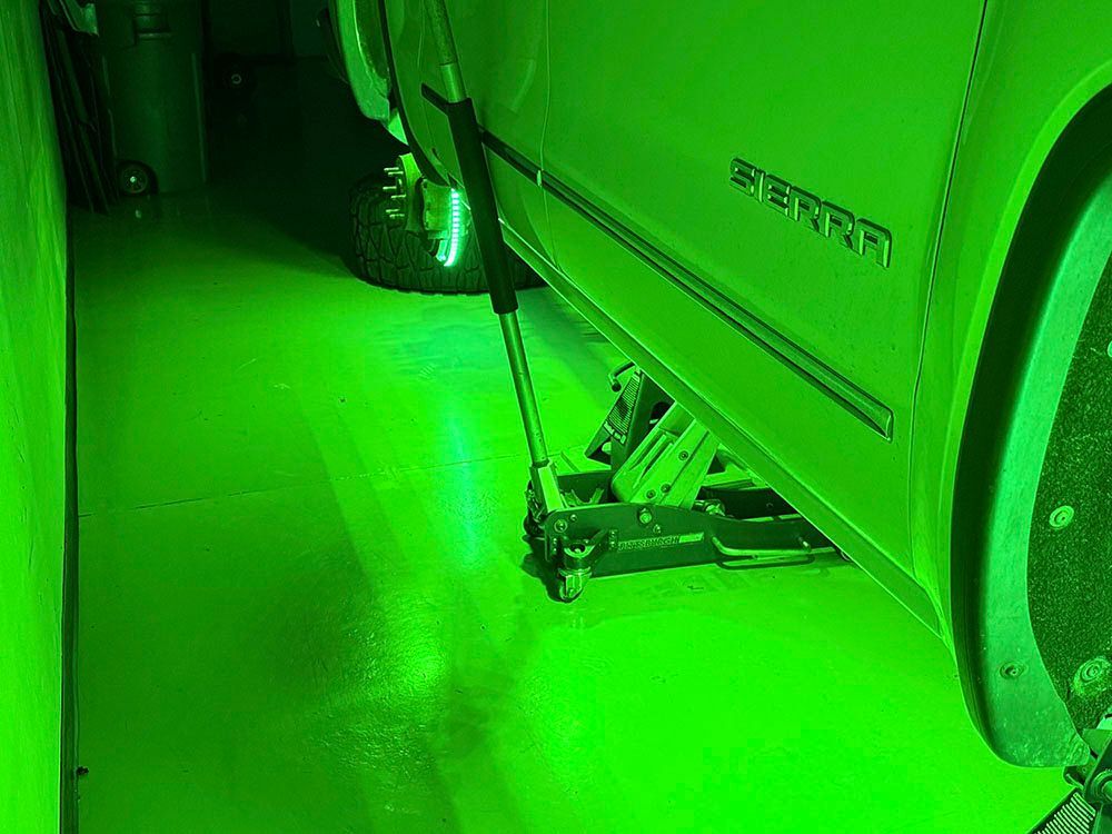 A white truck is jacked up on a green lit floor. The word 