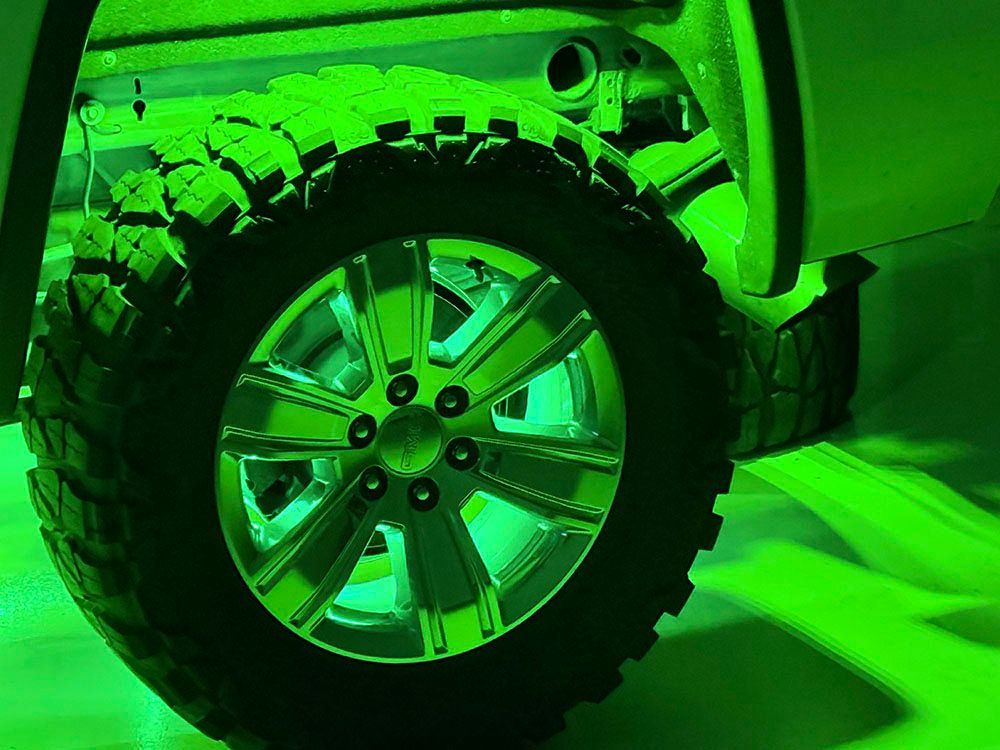 Green-lit off-road truck tire and chrome wheel, illuminated from underneath.