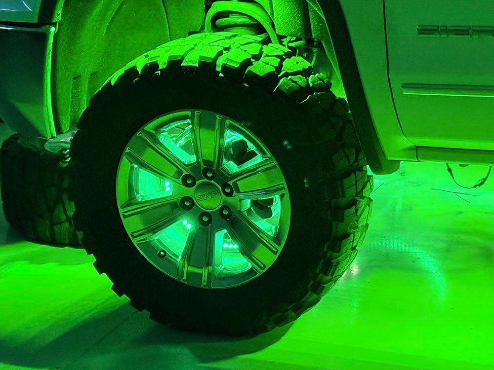 Green underglow illuminates a lifted truck wheel.