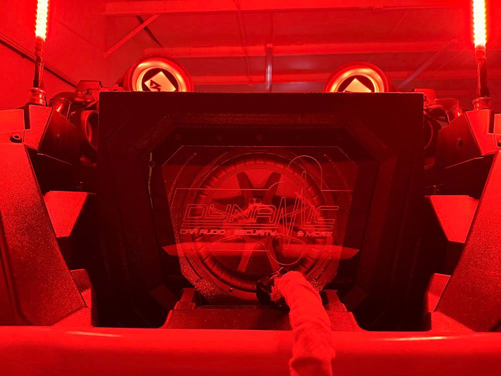 Red-lit car audio system, with a hand touching the subwoofer enclosure's logo.