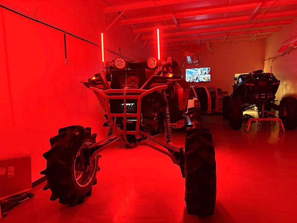 Red-lit room with large-tired ATV. Another ATV is partially visible on the right, both indoors.