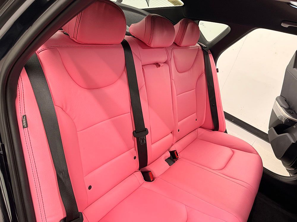Pink leather car backseat with black seatbelts.