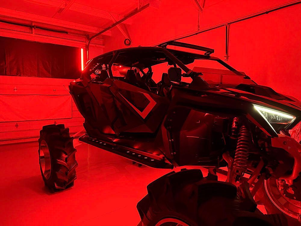 Black off-road vehicle with large tires, lit with red light inside a garage or building.