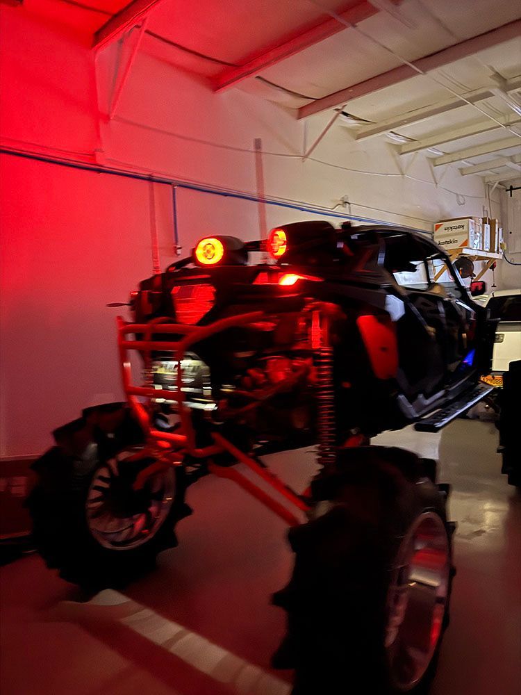 Black off-road vehicle with large tires, lit by red light in a white garage.
