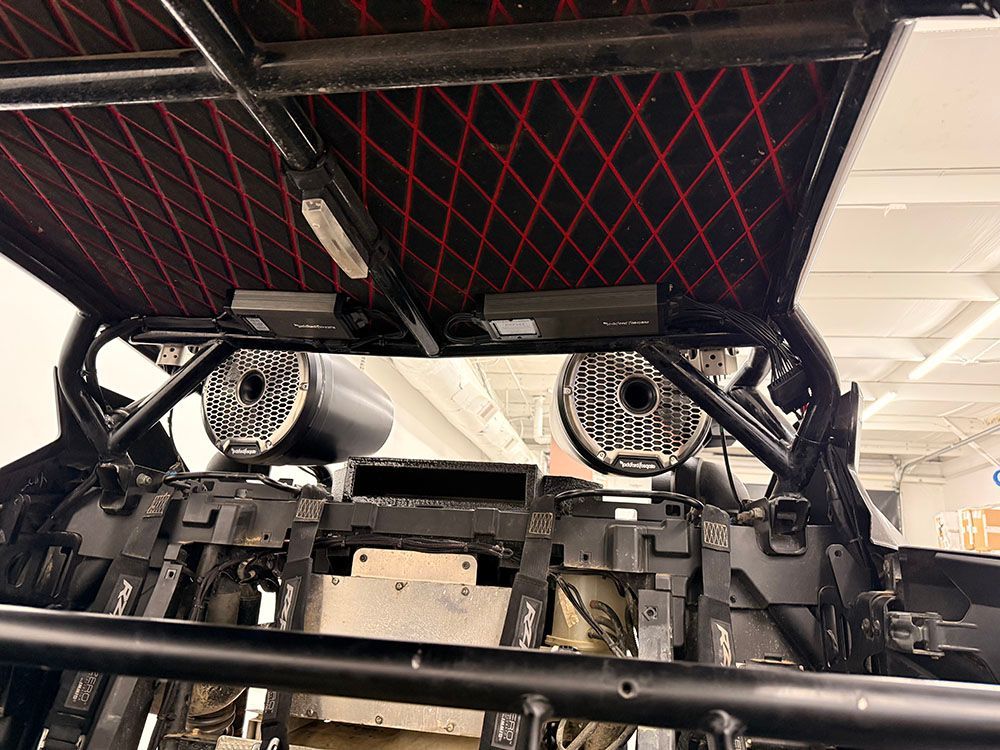 Black roll cage with a red-stitched headliner, speakers, and electronics mounted inside.