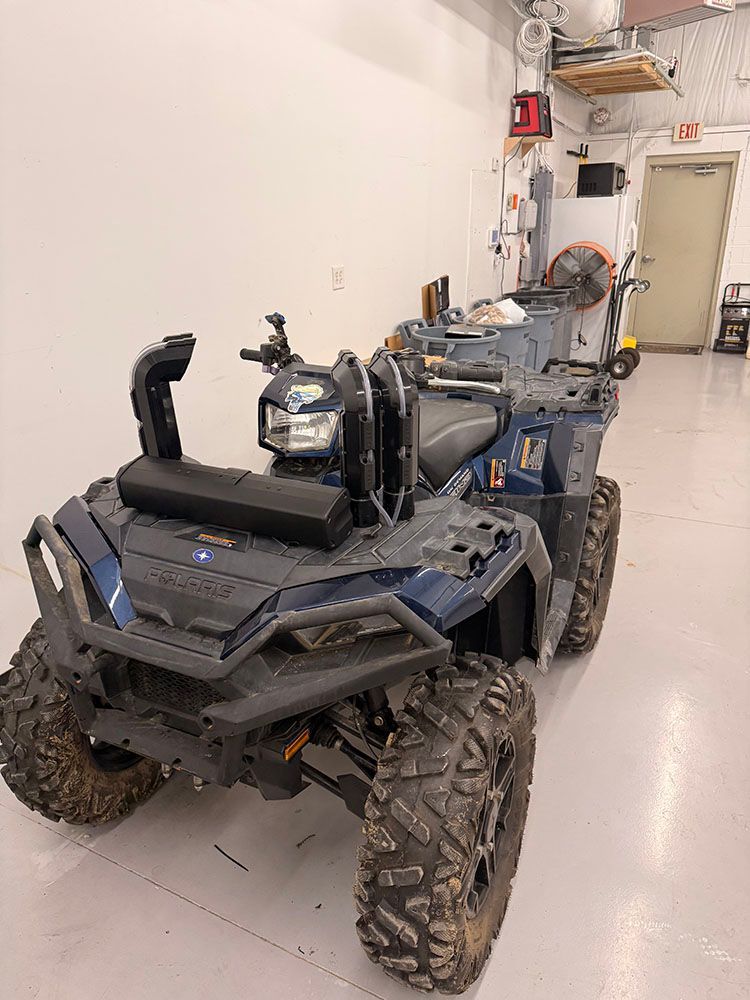 Dark blue ATV in a garage with large, mud-covered tires.