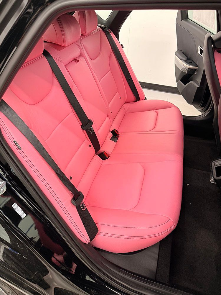 Pink leather car back seats with black seat belts in a black car interior.