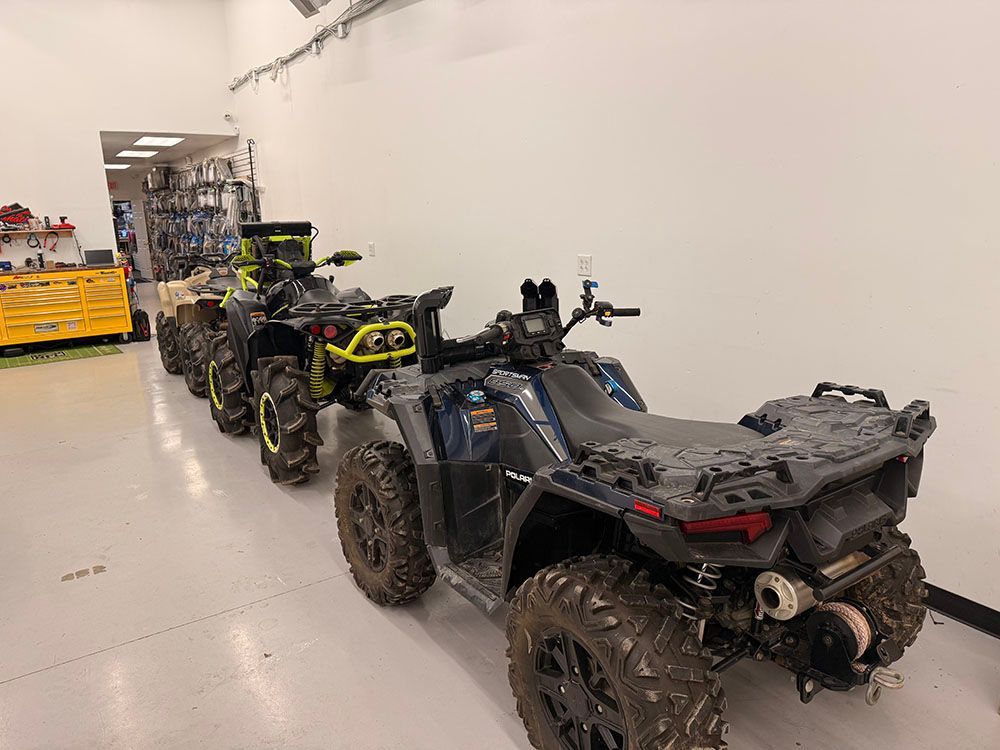 Several mud-covered ATVs parked in a row inside a bright garage.