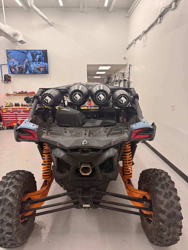 Rear view of a blue and black off-road vehicle with orange suspension. Features four lights on a roll cage.