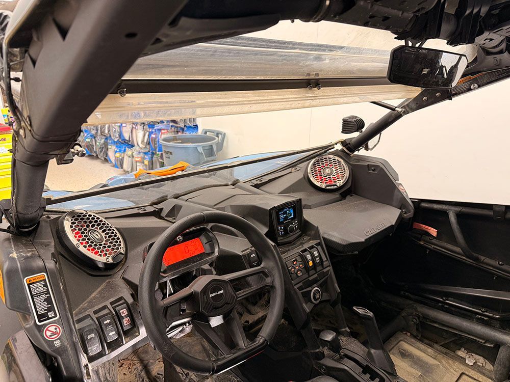 Interior view of a side-by-side vehicle with dashboard, steering wheel, and speakers.