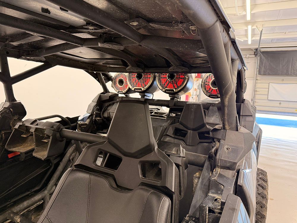Inside view of a black side-by-side with roll cage; speakers mounted overhead.