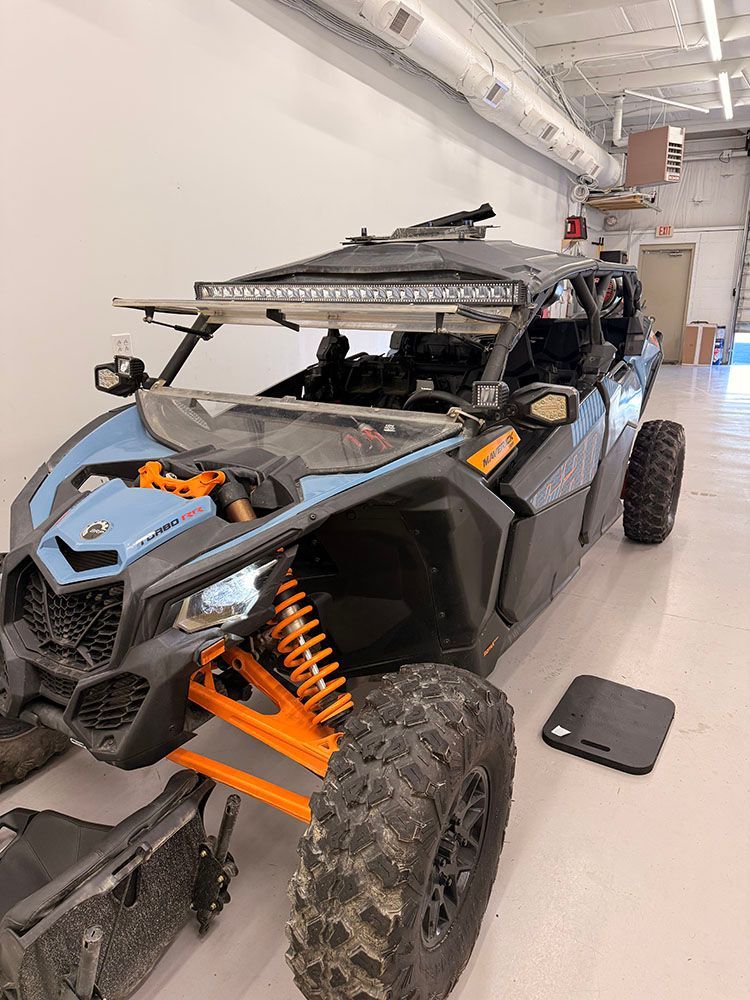 Blue and black off-road vehicle with orange suspension, LED light bar, parked indoors.