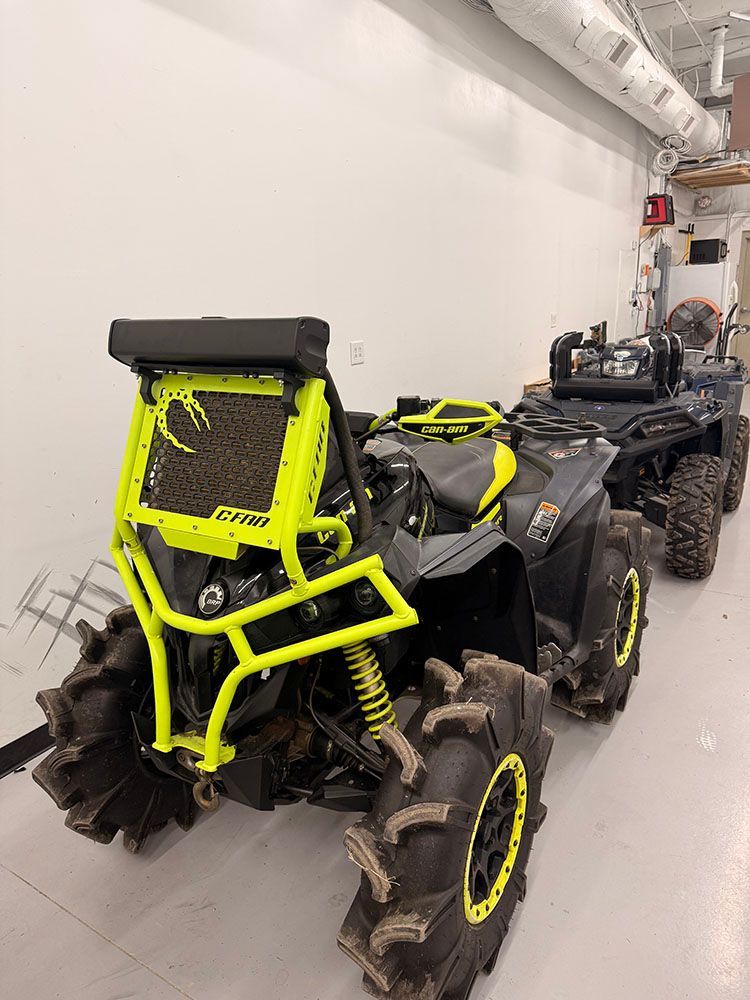 Two modified ATVs with large mud tires, one bright yellow, parked indoors.