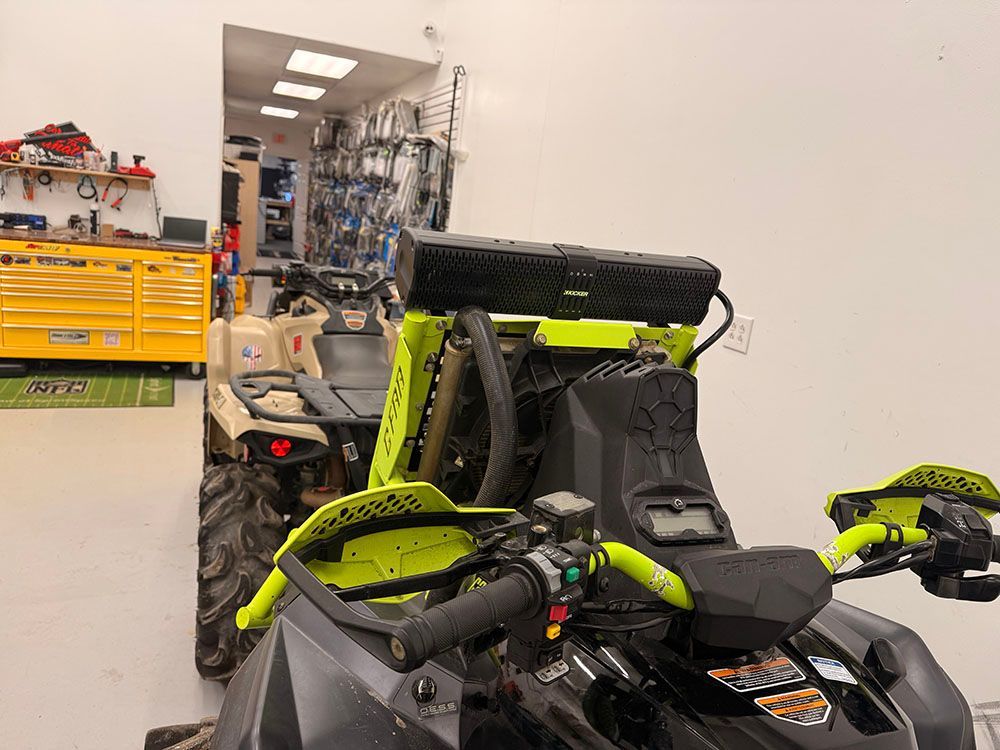 Black and lime green ATV indoors, next to another ATV in a shop. Tools and supplies in the background.