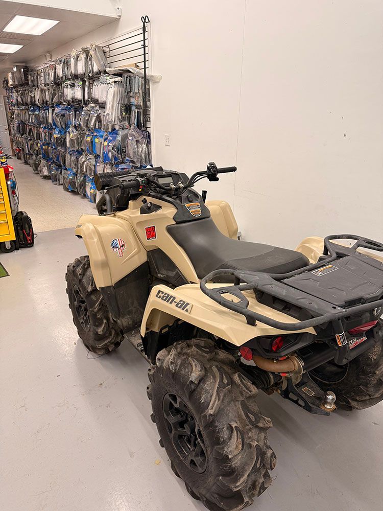 Tan ATV with large tires parked inside a shop with parts on the wall.