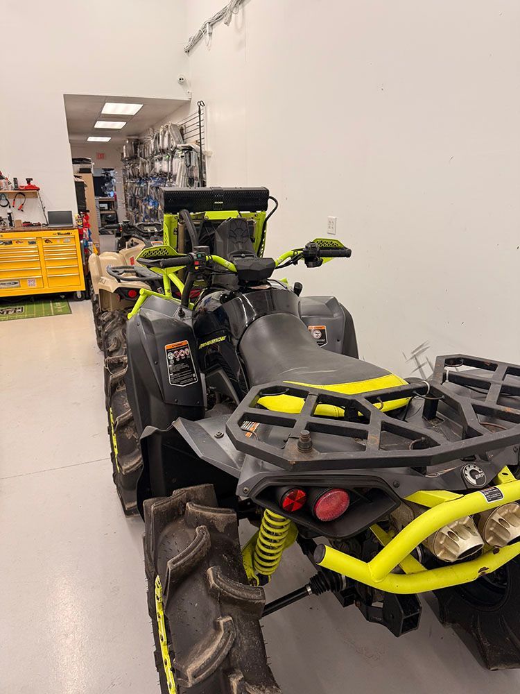 Black and neon-yellow ATV in a showroom; black tires, luggage rack, and accessories.