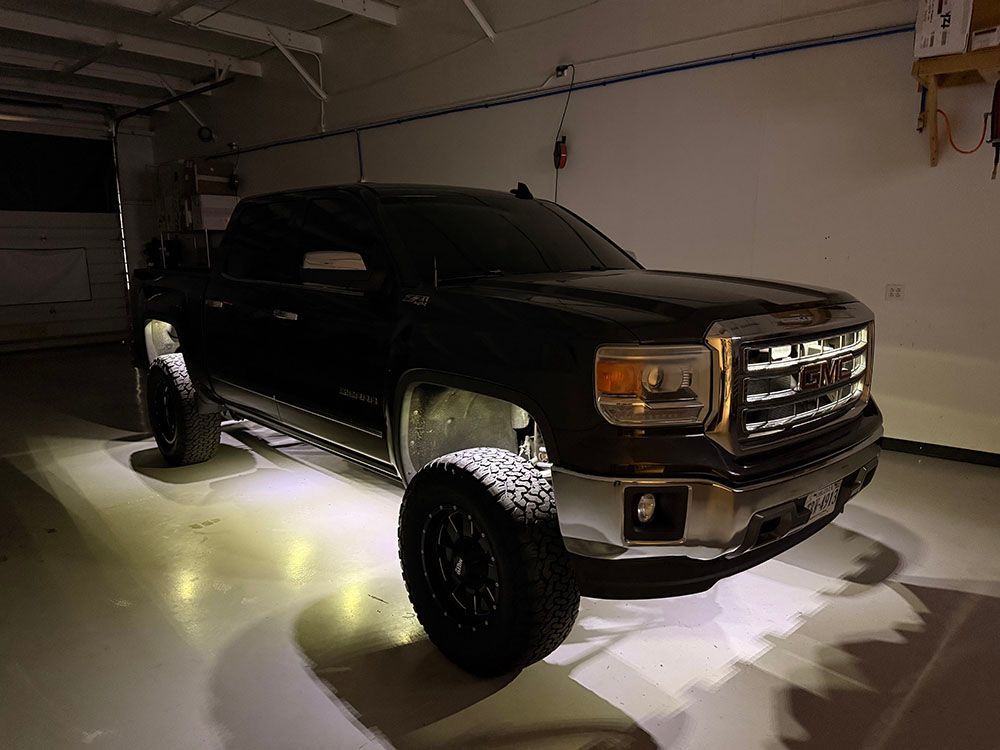 Black lifted GMC truck with bright underglow lights in a garage.