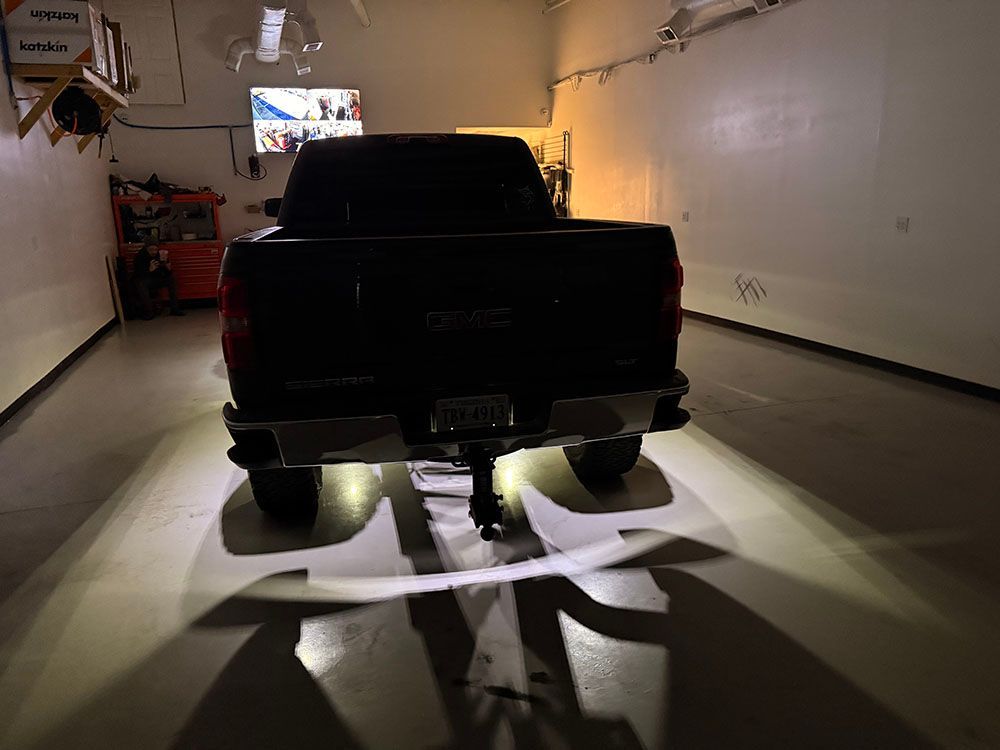 Dark pickup truck inside a garage with bright lights under it, casting shadows.