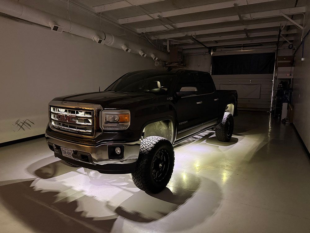 Black GMC truck parked in a garage with underglow lighting.