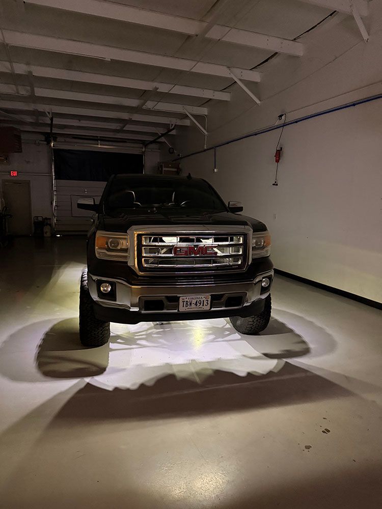 Black GMC truck with bright headlights, inside a white garage.