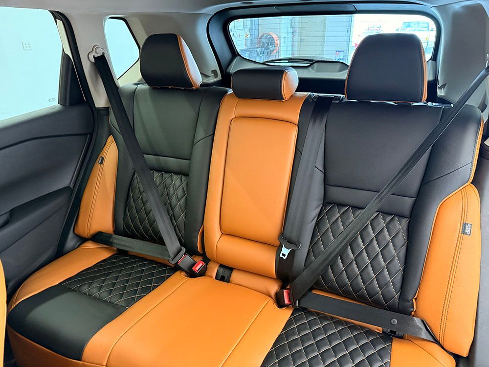 Rear car seats: black and orange leather upholstery with seatbelts, inside a vehicle.