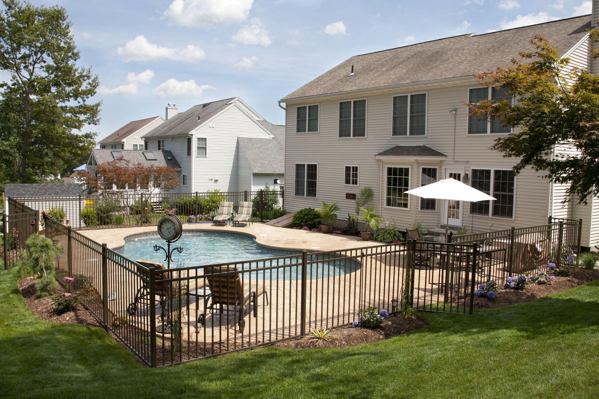 Backyard swimming pool with black fence, patio furniture, and two-story houses in the background
