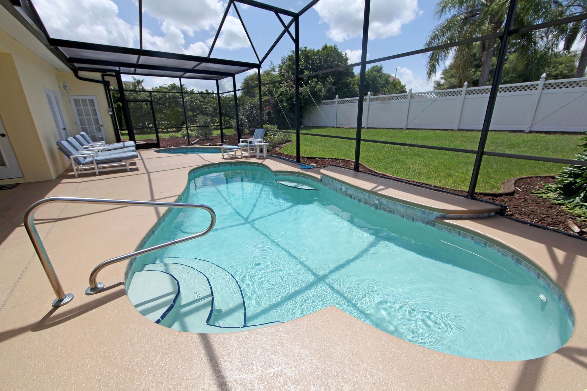 Backyard swimming pool with handrail, screened enclosure, lounge chairs, and grassy fenced yard