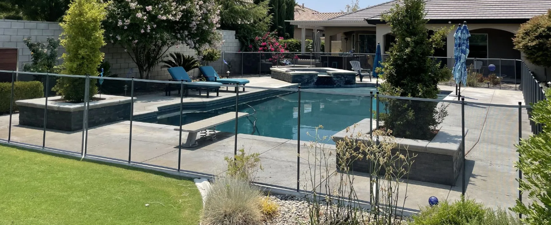 Backyard pool with a fenced patio, lounge chairs, and landscaped plants under a sunny sky