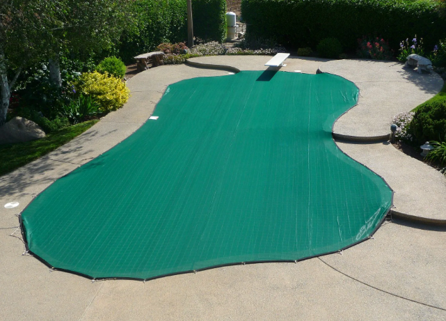 Green pool cover over an outdoor in-ground pool, surrounded by concrete patio and garden greenery