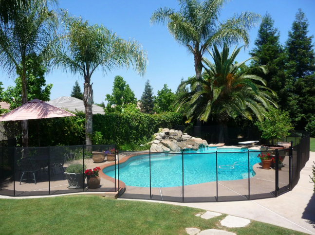 Backyard pool with palm trees, patio fencing, and a clear blue swimming area under sunny skies