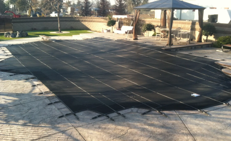 Backyard patio covered with black mesh, surrounded by a house, lawn, and garden seating.