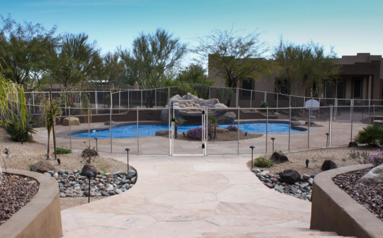Desert backyard with a fenced blue swimming pool and rock landscaping