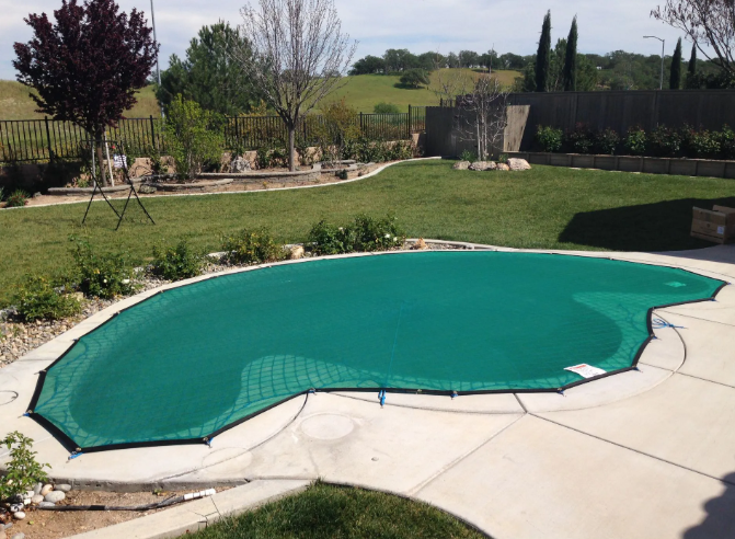 Covered backyard swimming pool with a teal tarp and concrete patio in a landscaped yard