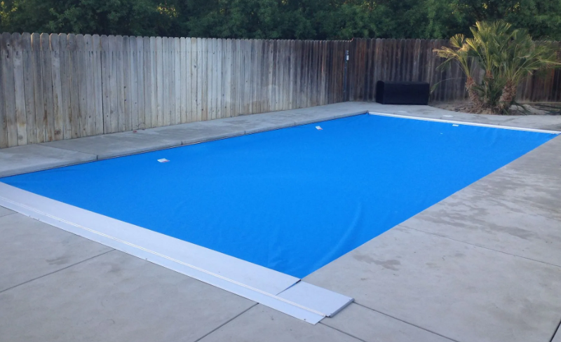 Covered rectangular backyard swimming pool with a bright blue safety cover