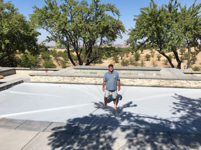 Man standing in a sunlit park near trees and a dry landscaped area