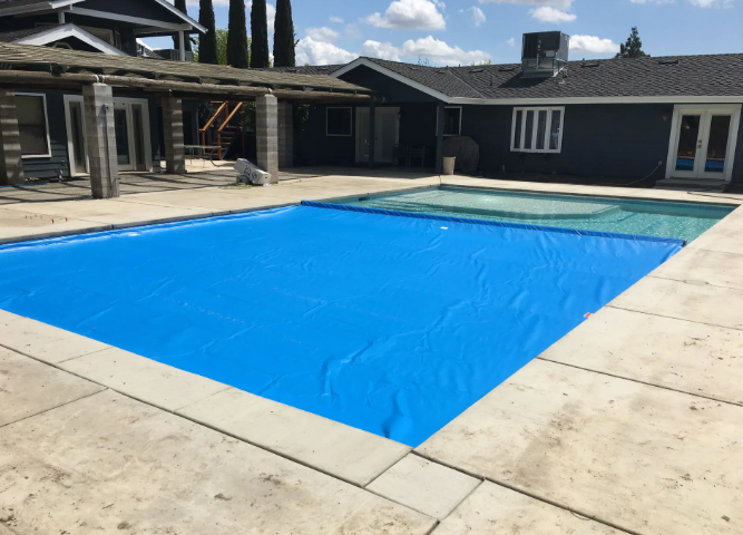 Backyard swimming pool covered with a bright blue tarp beside a house