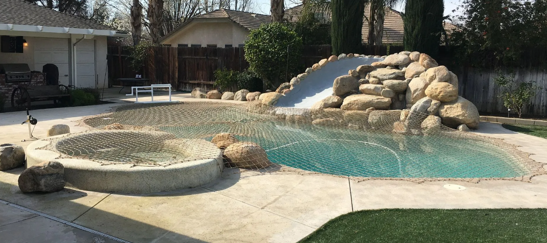 Backyard pool with turquoise water, rock waterfall, and stone patio beside a house