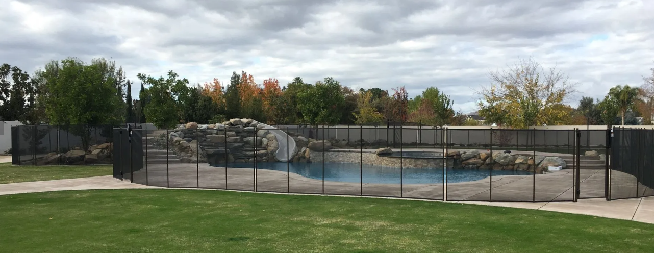 Outdoor park with fenced shallow pool, rock features, and grassy foreground under cloudy sky