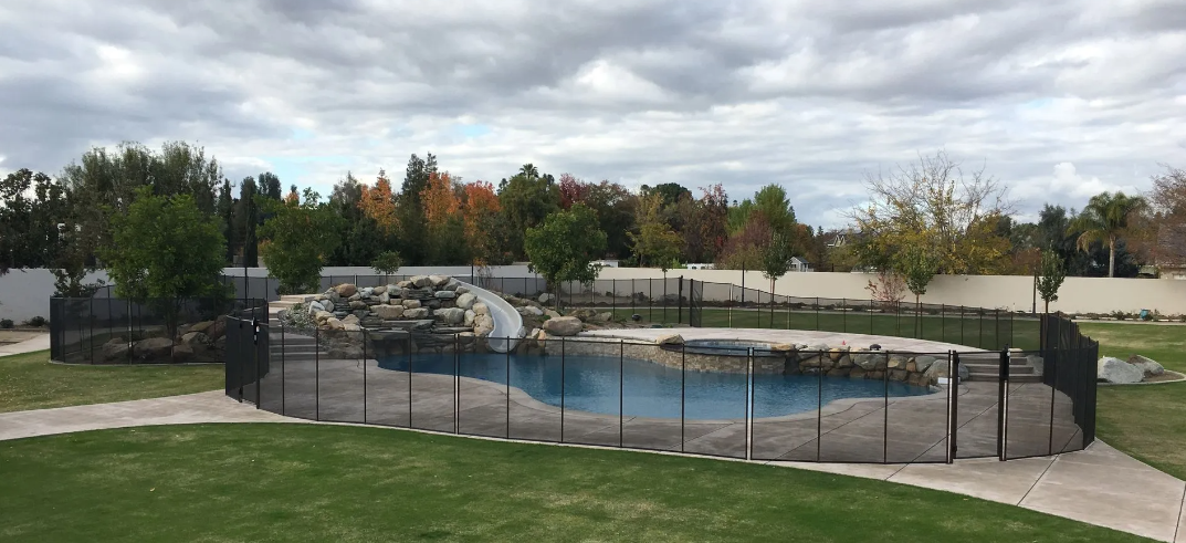 Outdoor zoo-like enclosure with a rocky pool, black fence, and green grass under cloudy sky